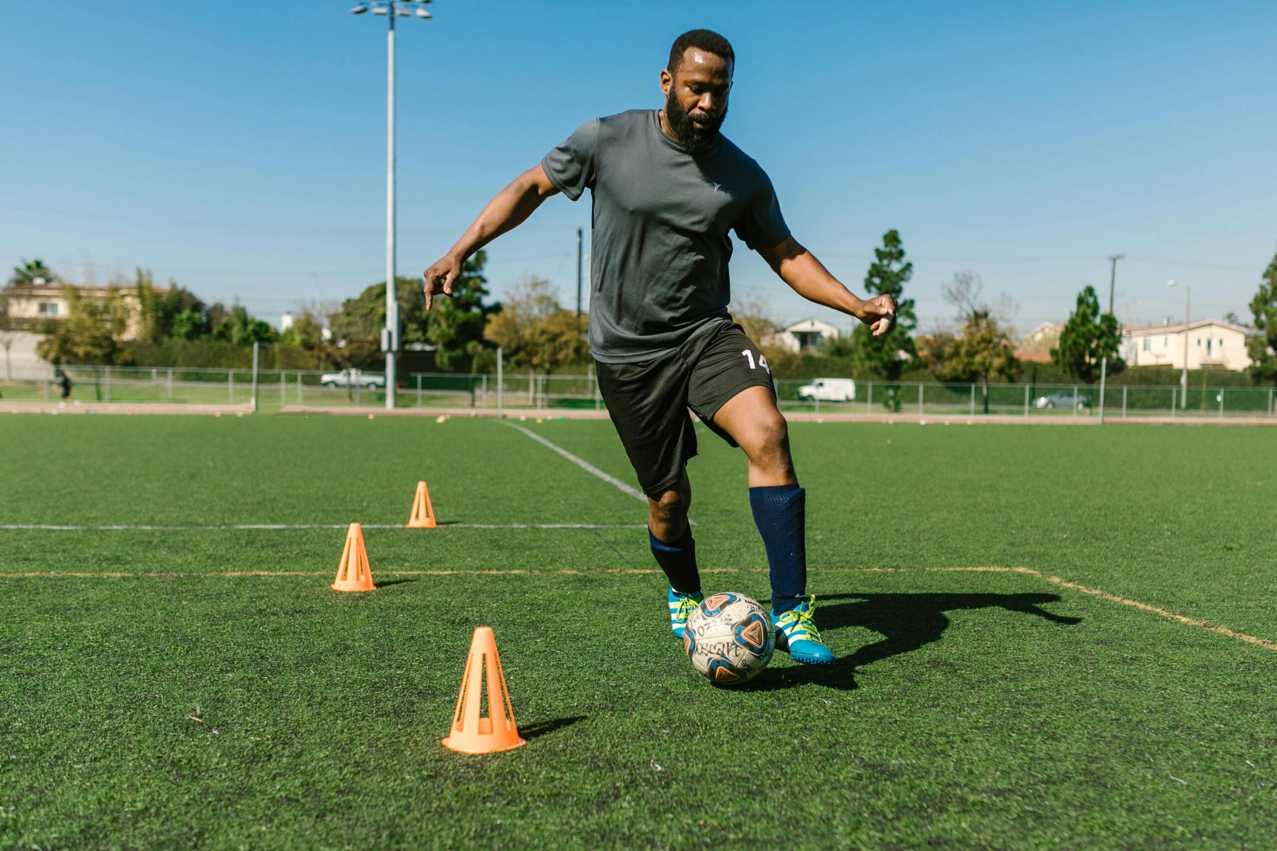 A man training on a soccer field, focused as he practices dribbling drills on the grass with cones set up around him.
