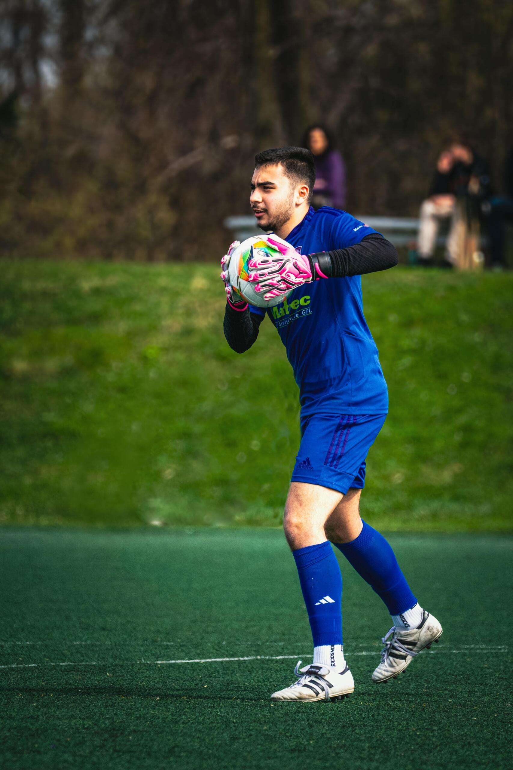 A man in a soccer uniform standing confidently on a field while holding a soccer ball under one arm, ready for the game.