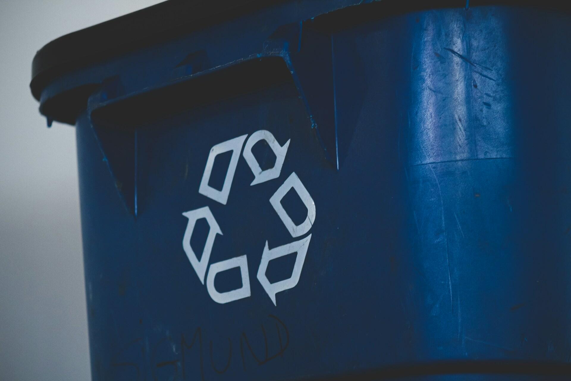 Close-up of a blue recycling bin featuring the recycling symbol prominently displayed on its side.