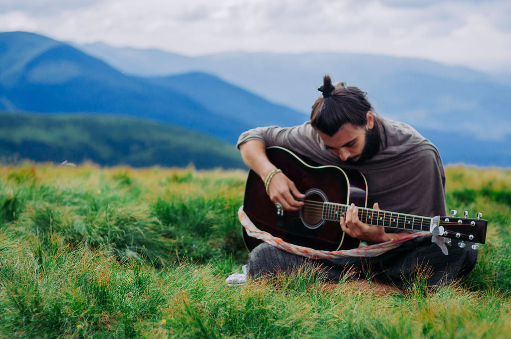 A man sits in a field playing guitar.