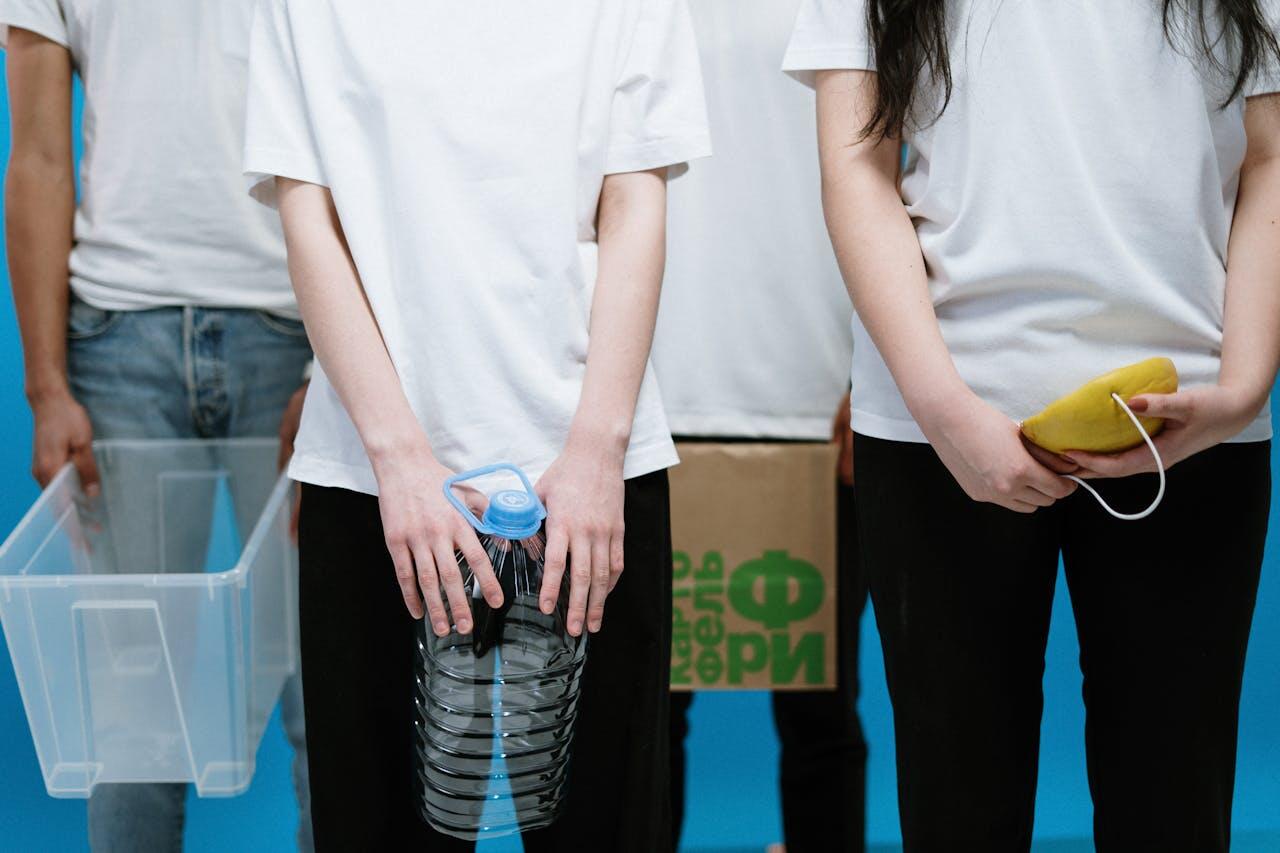A group of individuals in white shirts stands against a blue backdrop, holding a large water bottle, a transparent container, and a pouch.
