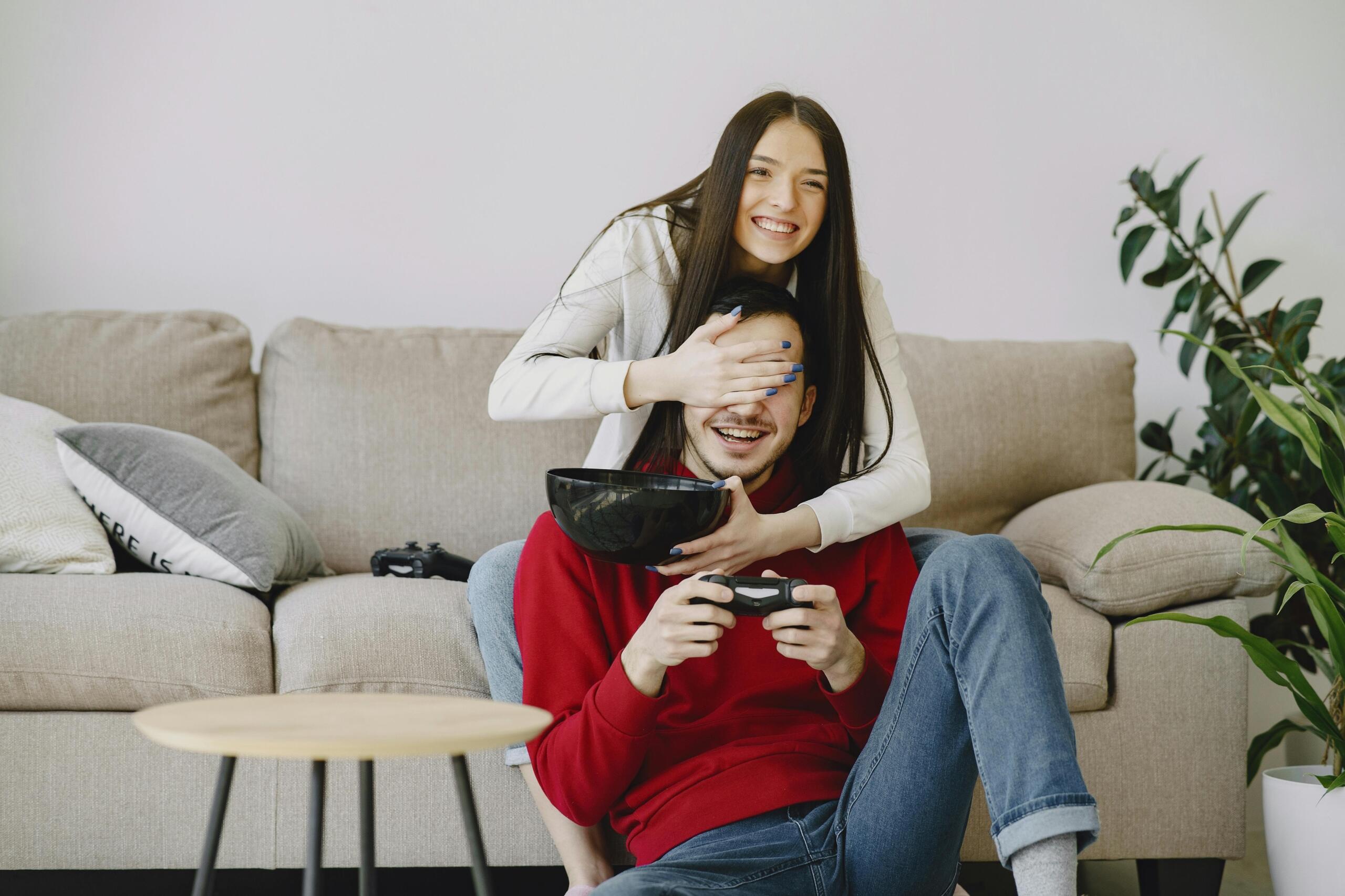 Smiling couple sitting on a couch playing video games together, each holding a game controller. 