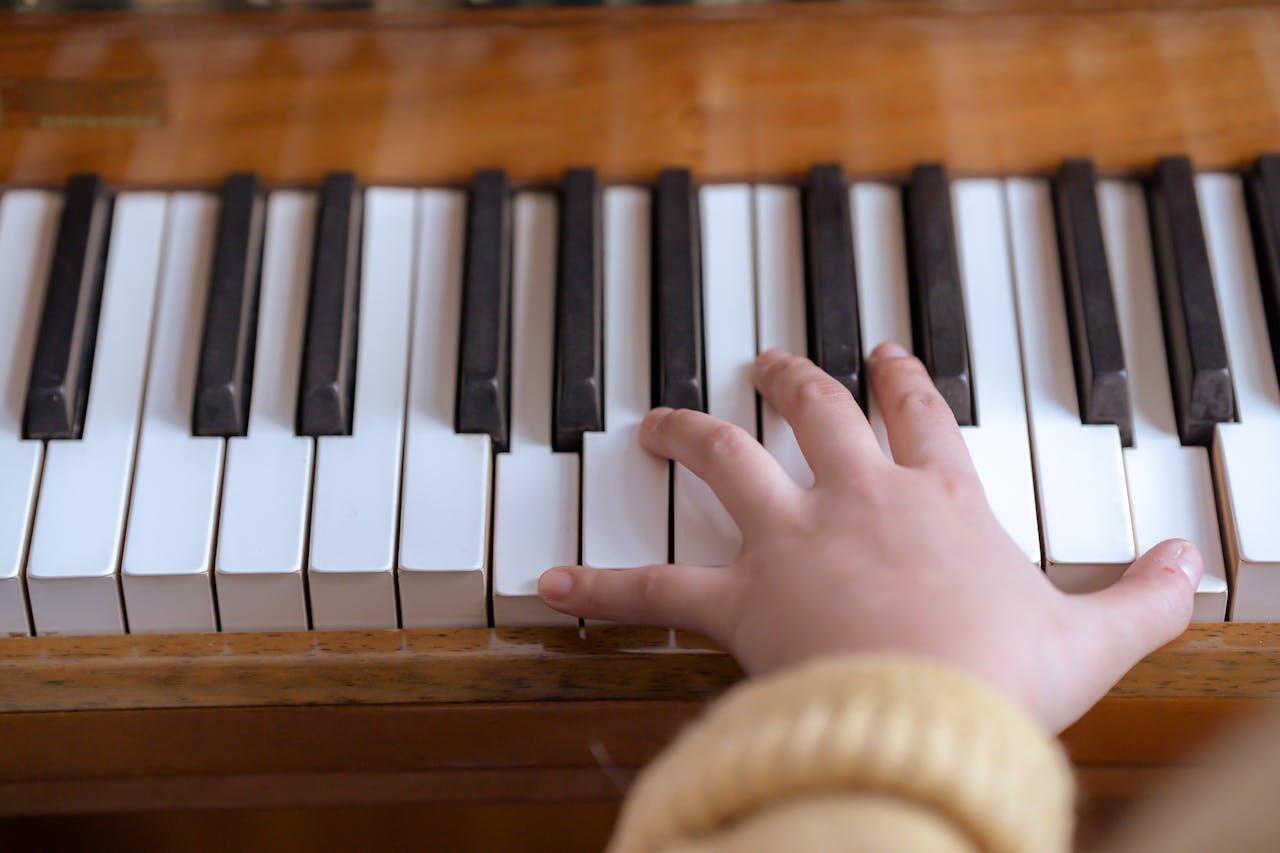 A child's hand pressing down on piano keys, with a focus on the black and white keys of a wooden piano.