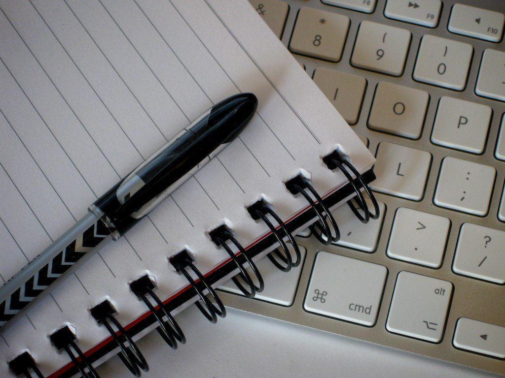 A notepad and pen next to a laptop. You can write poetry in a number of different ways.