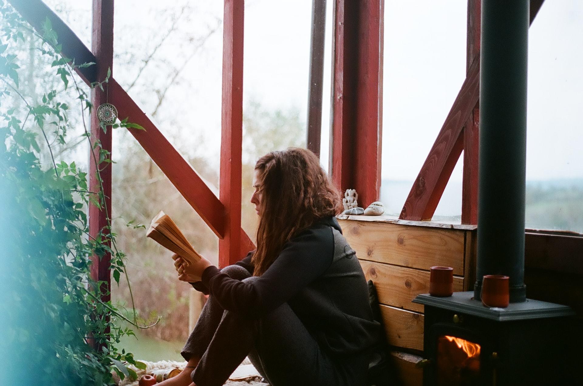 woman reading by a fireplace and window