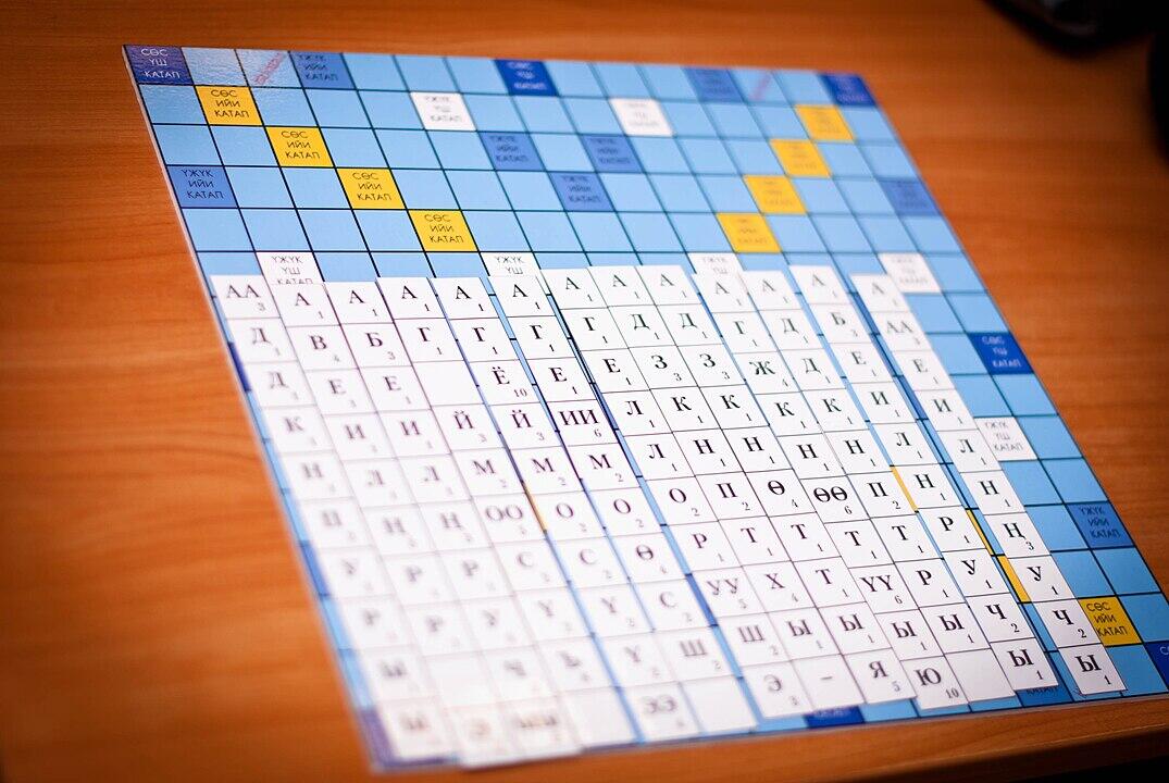 A close-up of a blue and white board game featuring Cyrillic letters and words, arranged in a grid format on a wooden table.