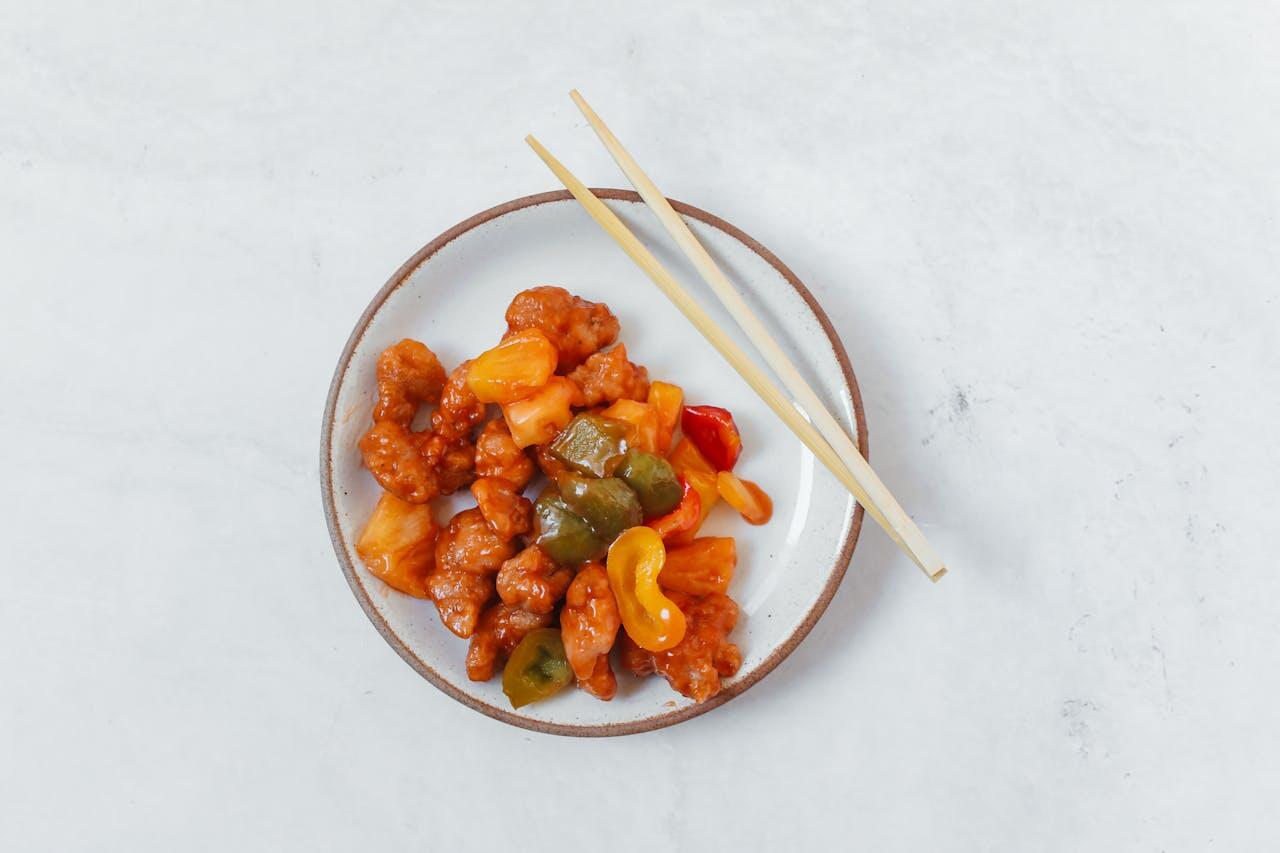 A plate of sweet and sour chicken with colorful bell peppers and pineapple, accompanied by chopsticks.