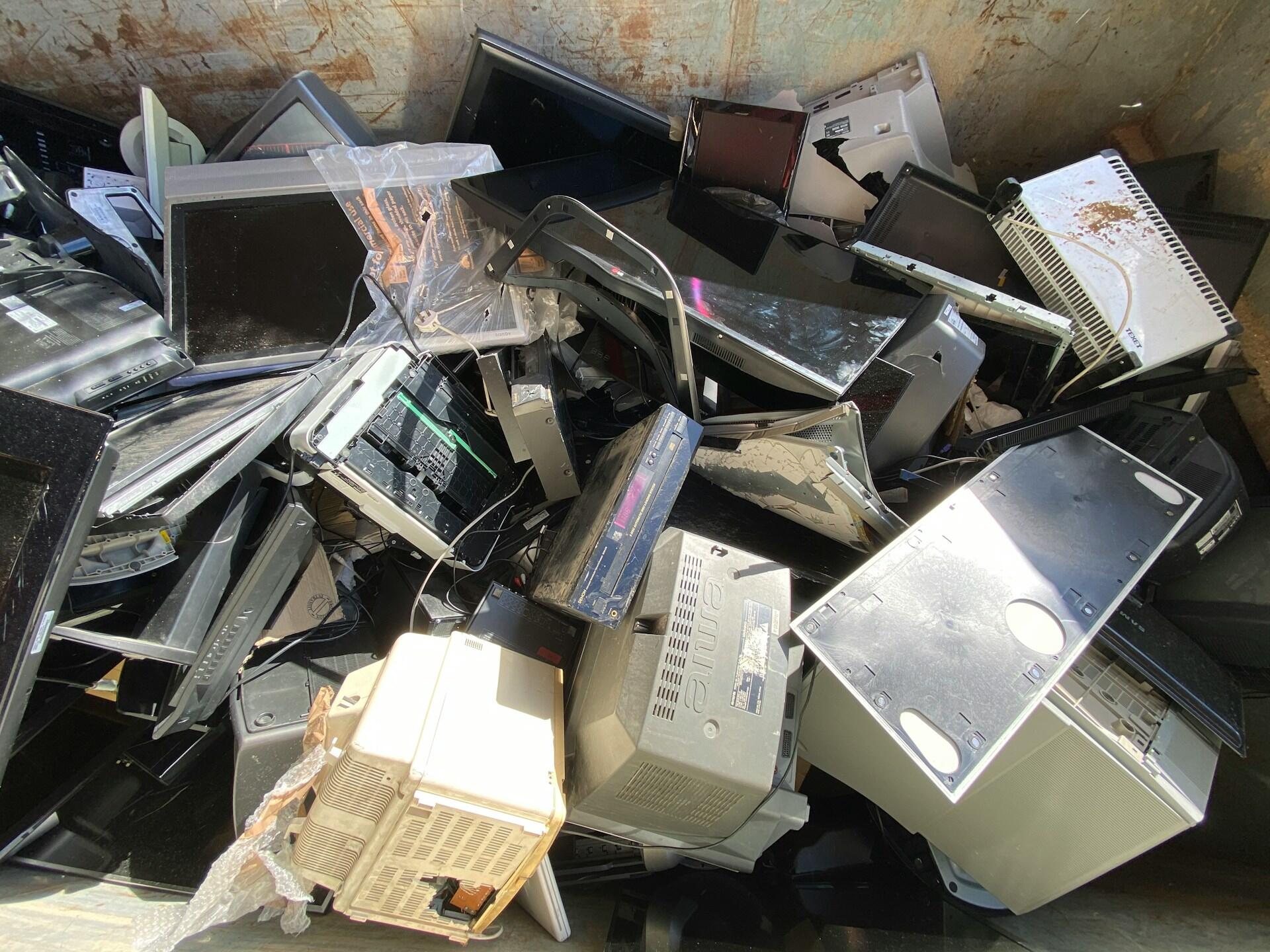 A chaotic pile of discarded electronic waste, including old monitors, computer towers, and cables, in a dumpster.