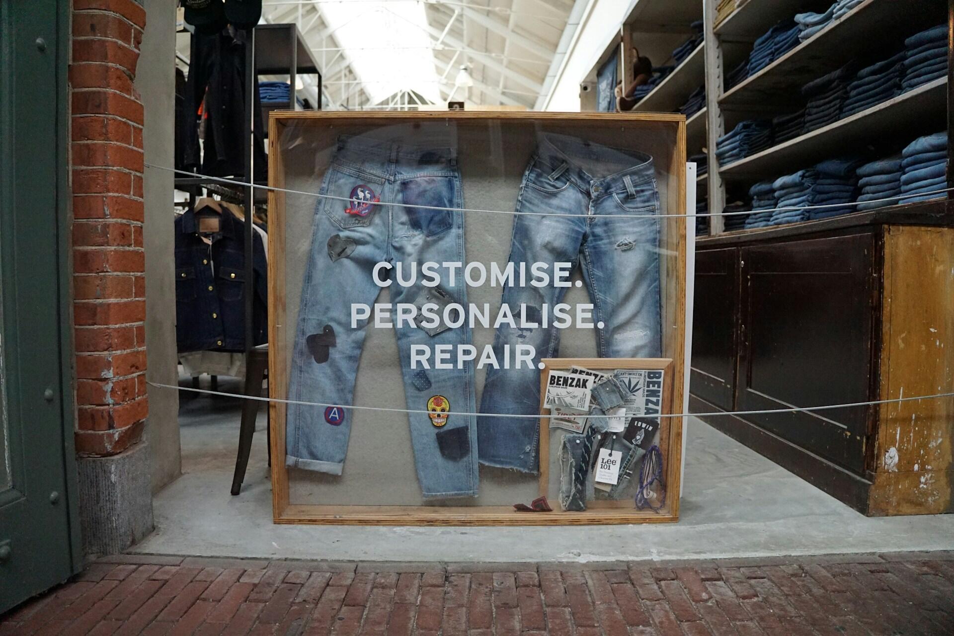 Display featuring customized jeans with patches, alongside a sign reading 