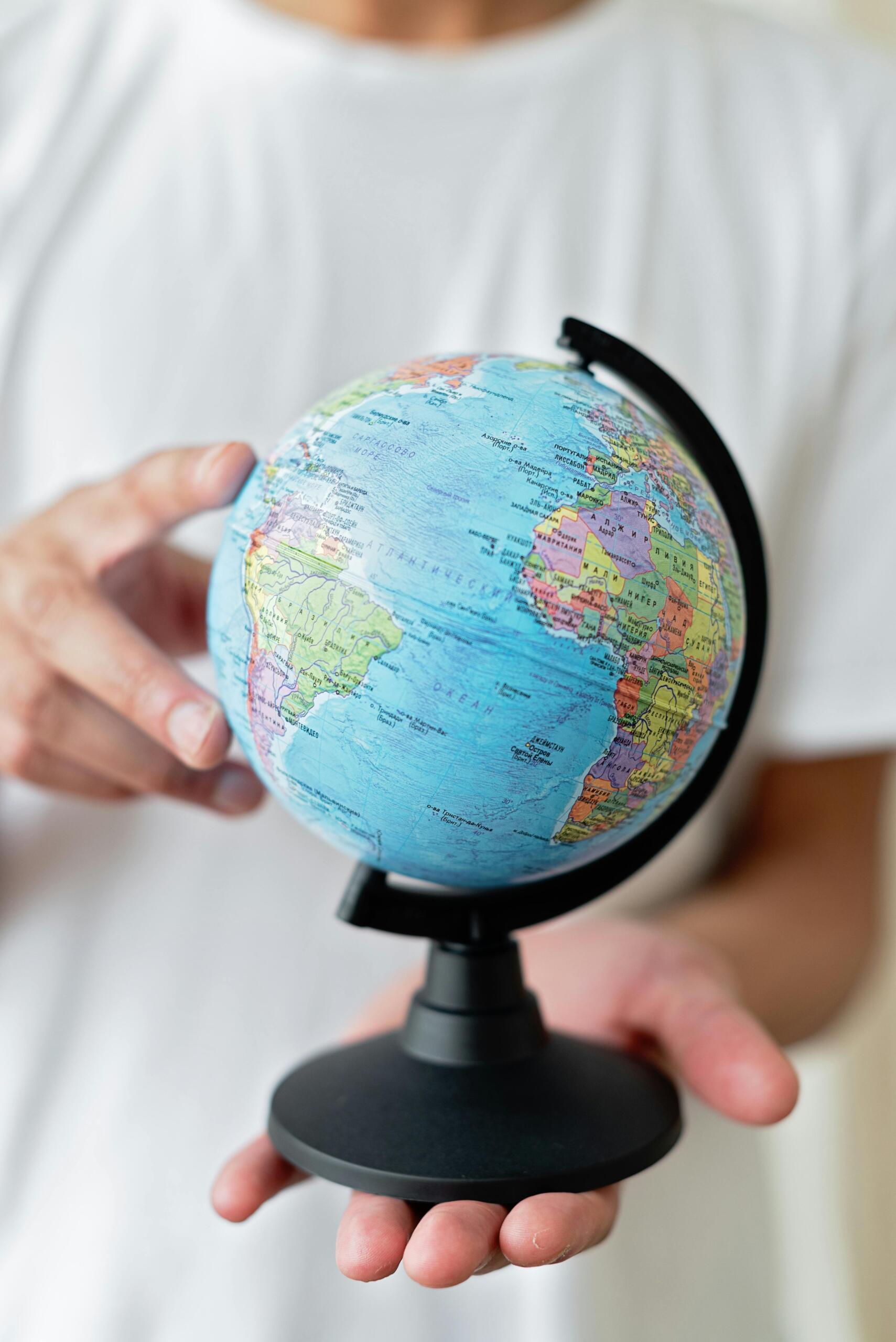 A person holding a small globe in their hand while supporting it on the side with two fingers.