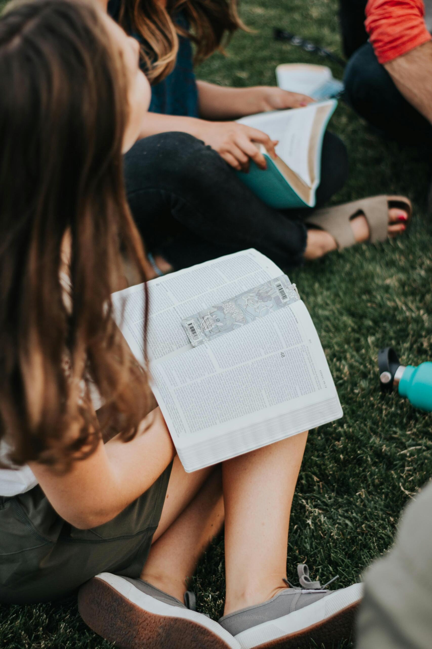 Students sitting on grass studying books together during an outdoor group study session.