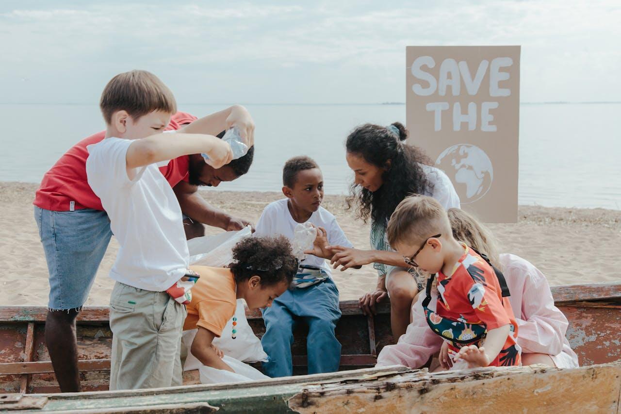 Children and adults gather on a beach, participating in an environmental cleanup project, with a "Save the Earth" sign in the background.