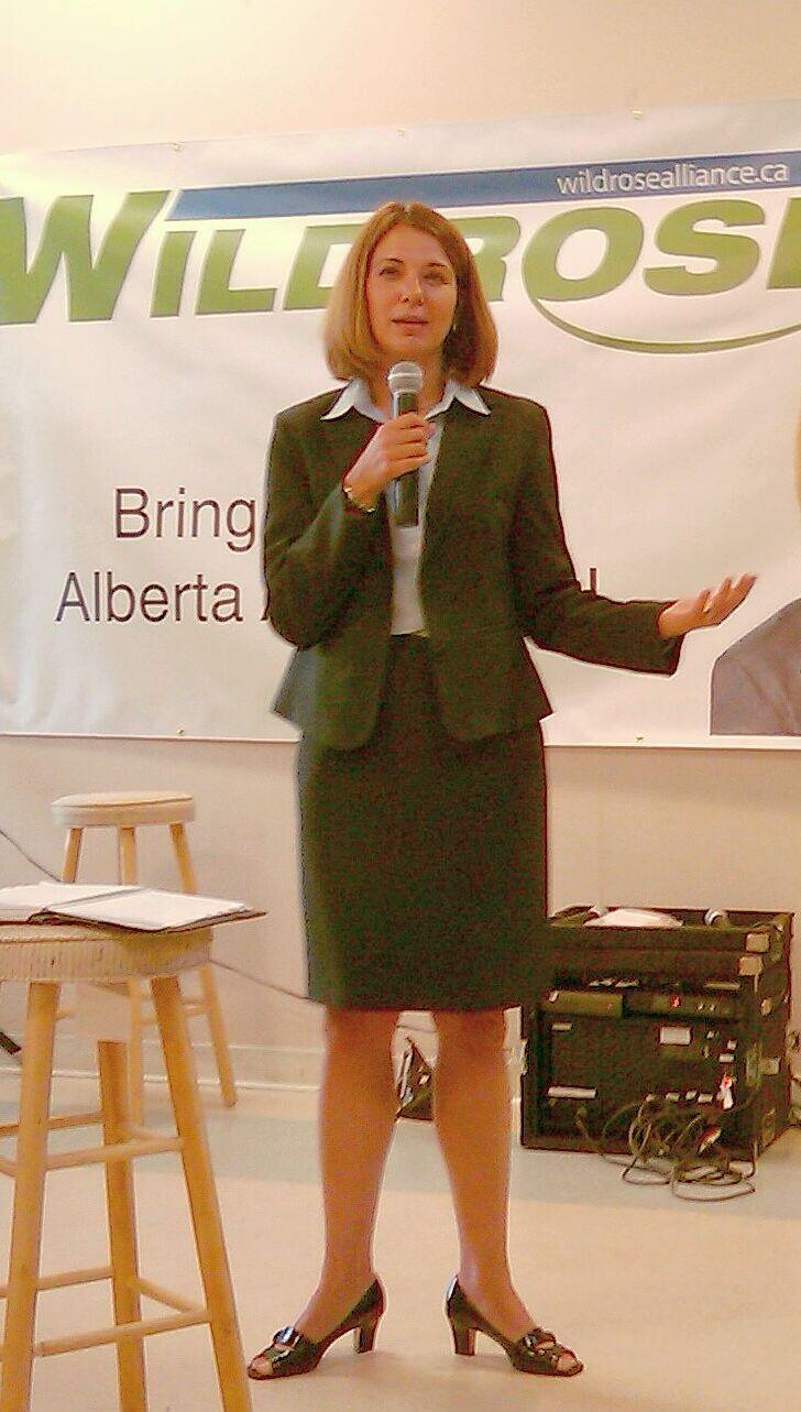 A photo of politician Danielle Smith when she campaigned for the Wildrose Party, now the UCP. She stands in front of a banner holding a microphone. Source: Wikimedia Commons.