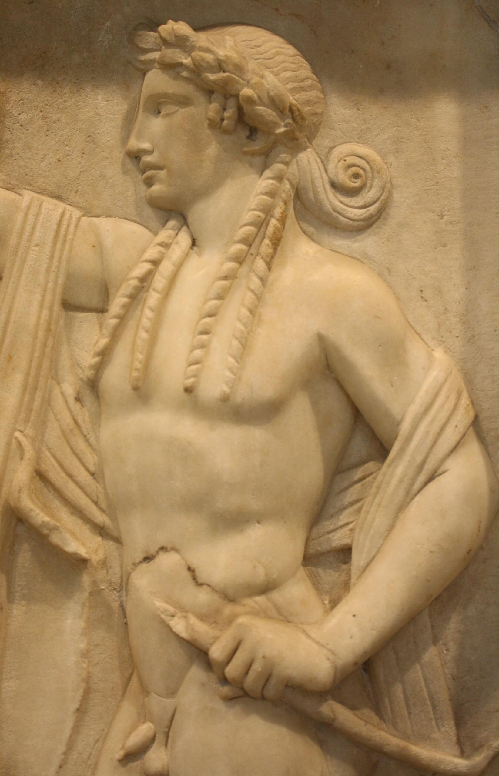 Marble relief of a muscular figure in ancient attire, holding a staff. The figure wears a laurel wreath, conveying a sense of dignity and strength.
