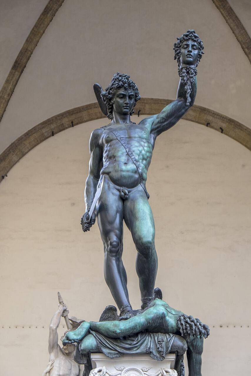 A bronze statue of a muscular nude man standing triumphantly on a pedestal, holding a severed head aloft in his right hand, conveying victory and strength.