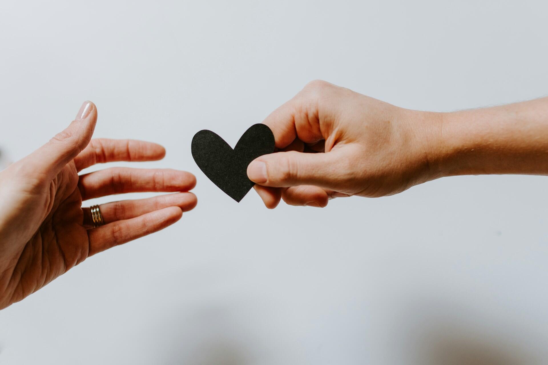 Two hands are sharing a small black heart against a light background, symbolizing love and connection.