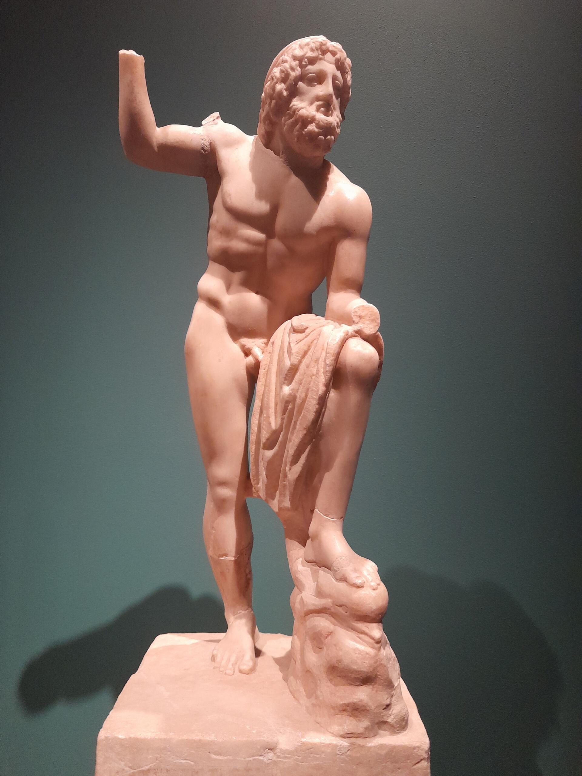 Marble sculpture of a bearded man with wavy hair, standing nude on a pedestal, draped cloth in one hand, conveys strength and classical elegance.