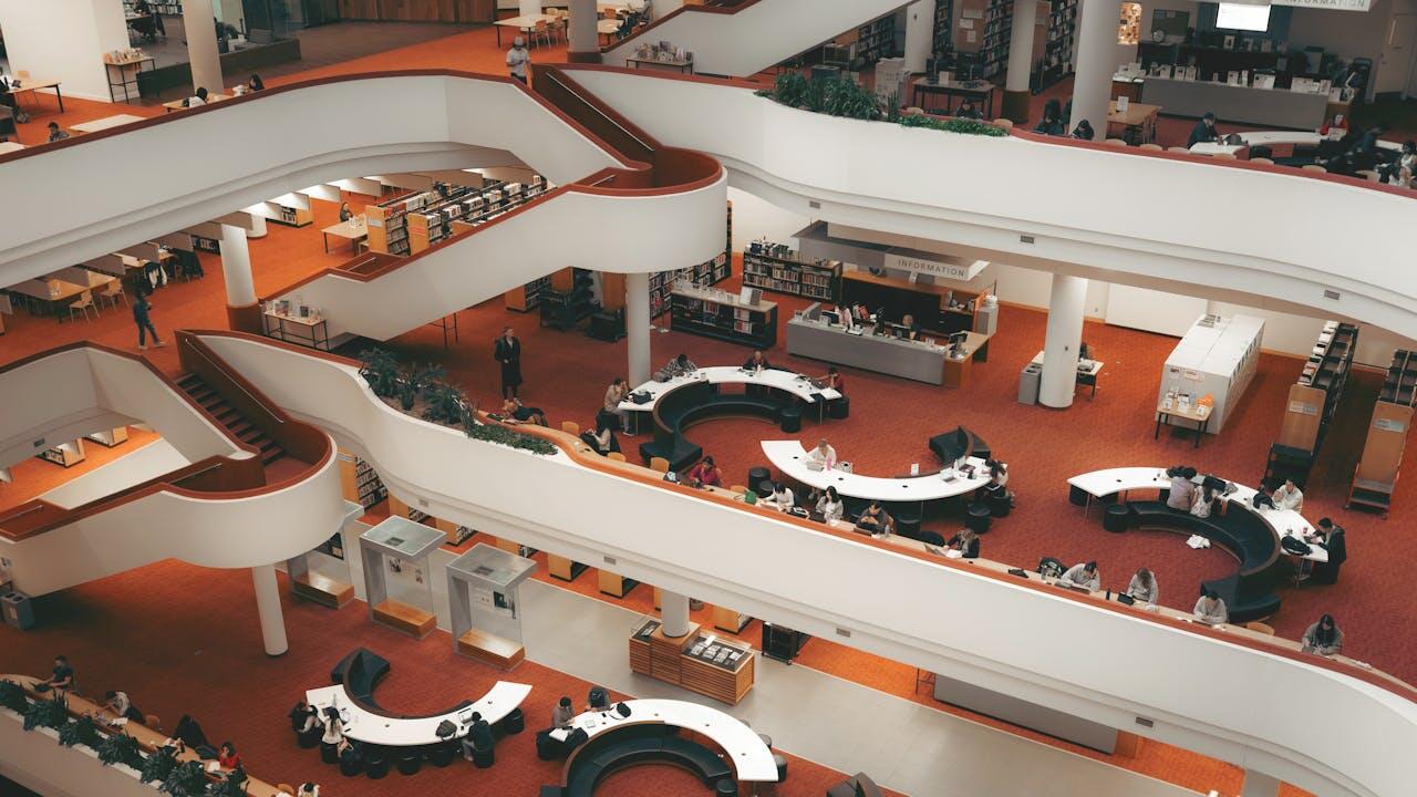 A modern library interior featuring multi-level floors, circular study tables, and patrons engaged in reading and studying activities.