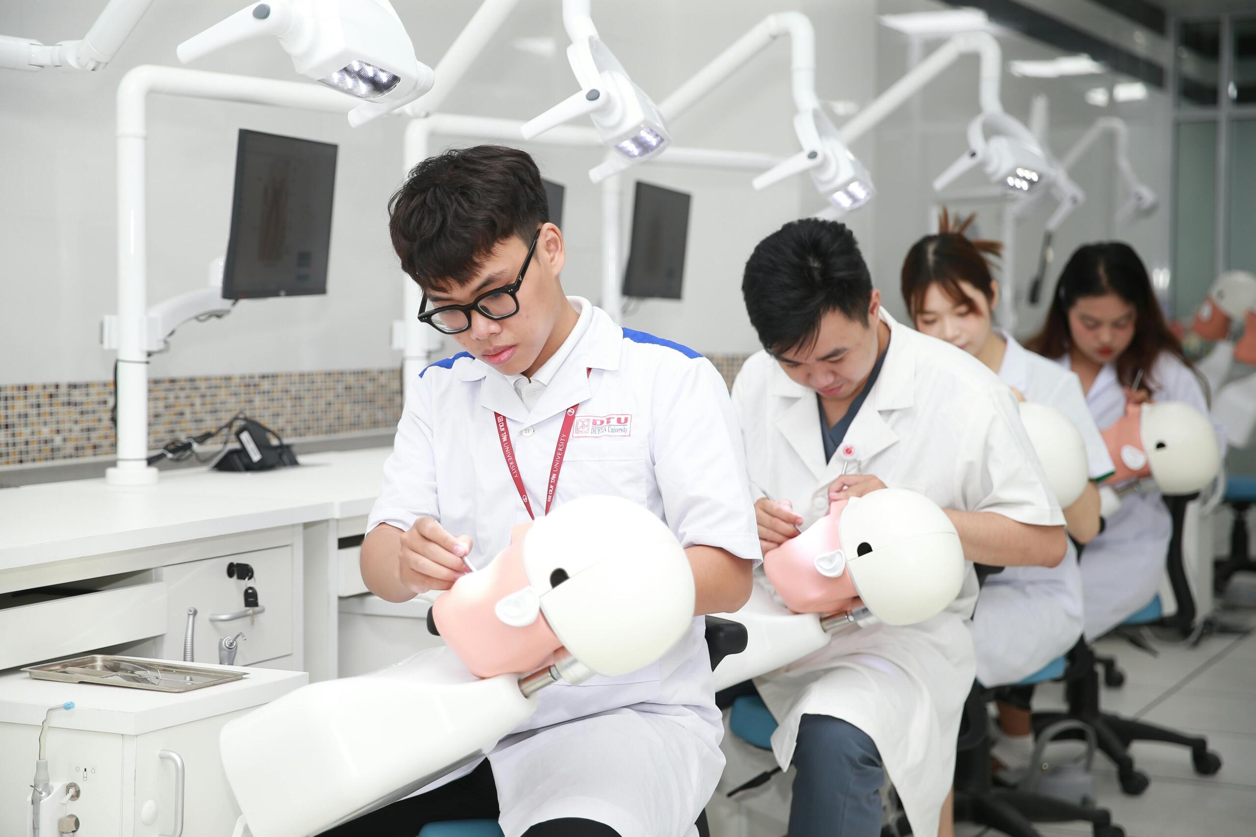 Students in dental training practice on mannequin heads in a modern classroom equipped with dental imaging screens.