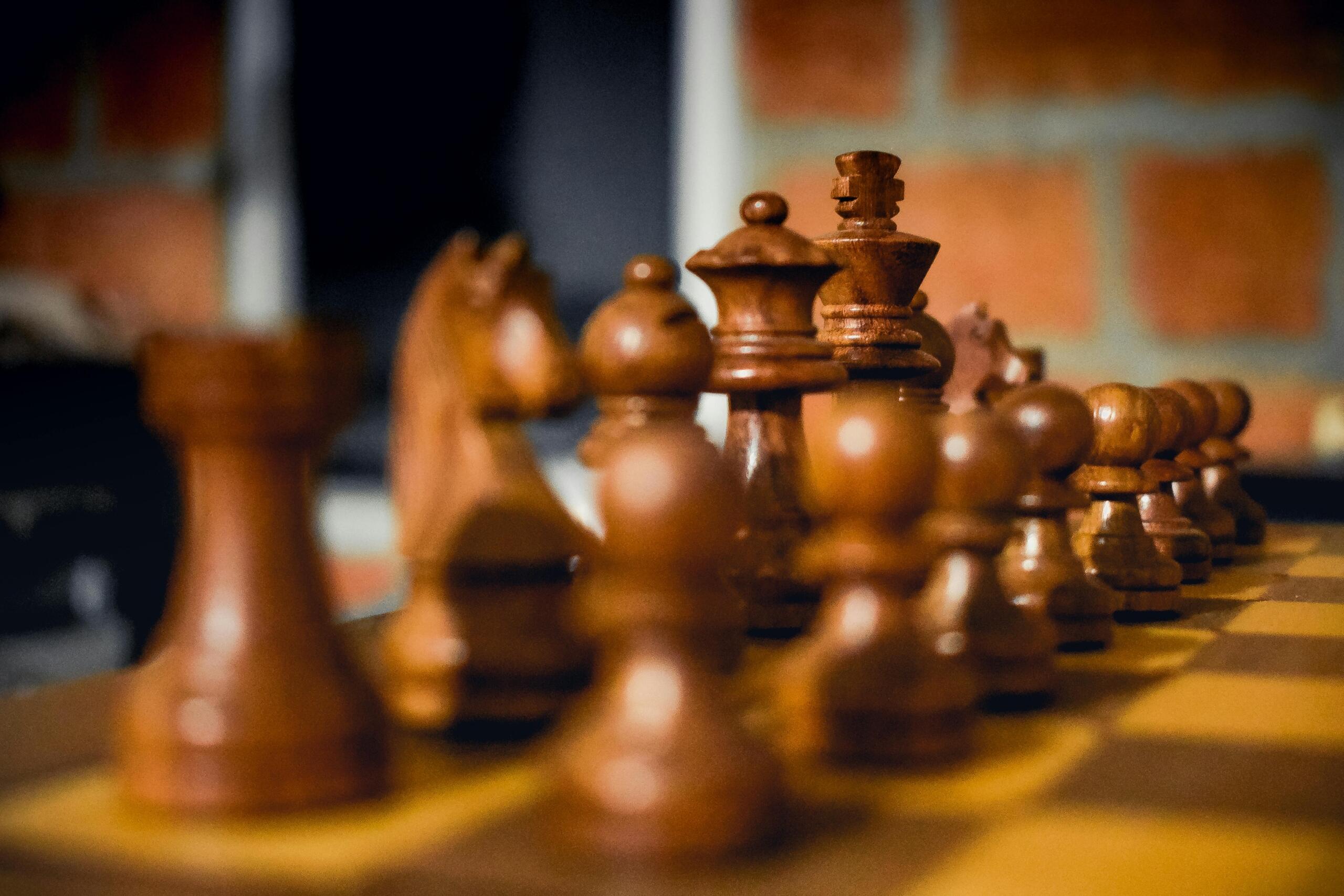 A close-up view of a chessboard with pieces arranged mid-game, showing the textured squares and detailed chess pieces in sharp focus.