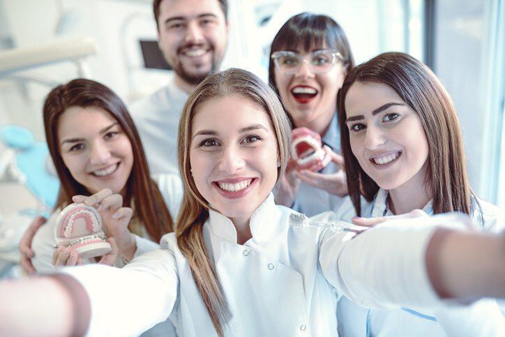 A group of dental professionals smiles for a selfie, showcasing dental models in a bright clinic setting.