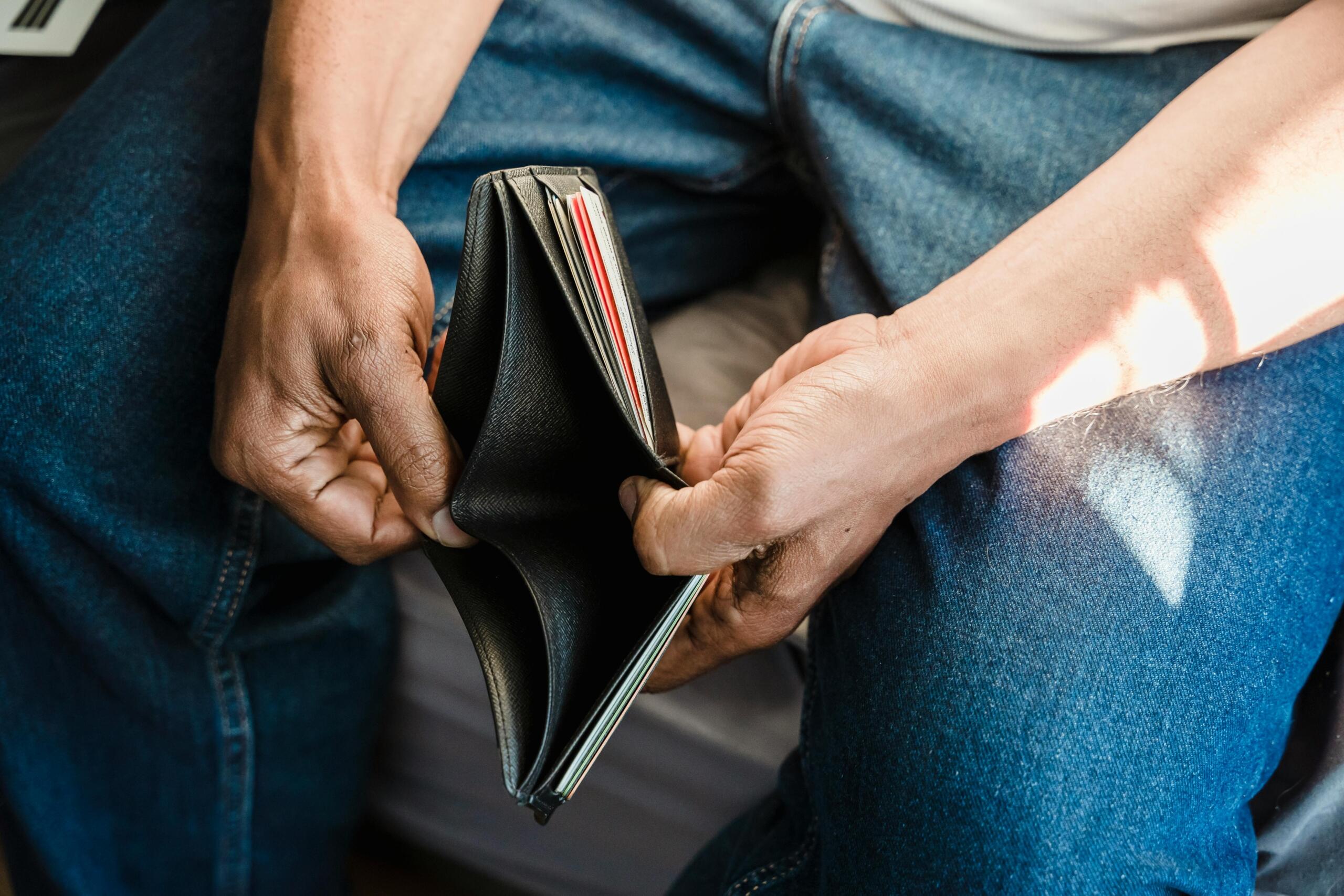 A person holding an empty wallet, revealing no cash or cards, while sitting in casual blue jeans.