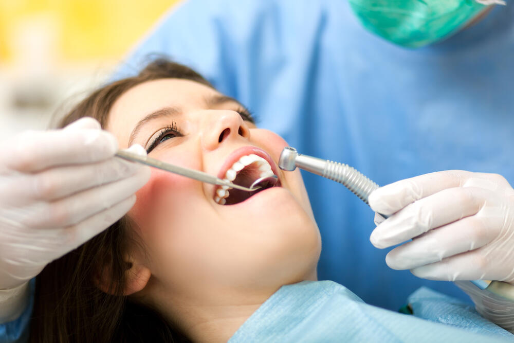 A dentist in gloves examines a patient's mouth with dental tools in a clinical setting.