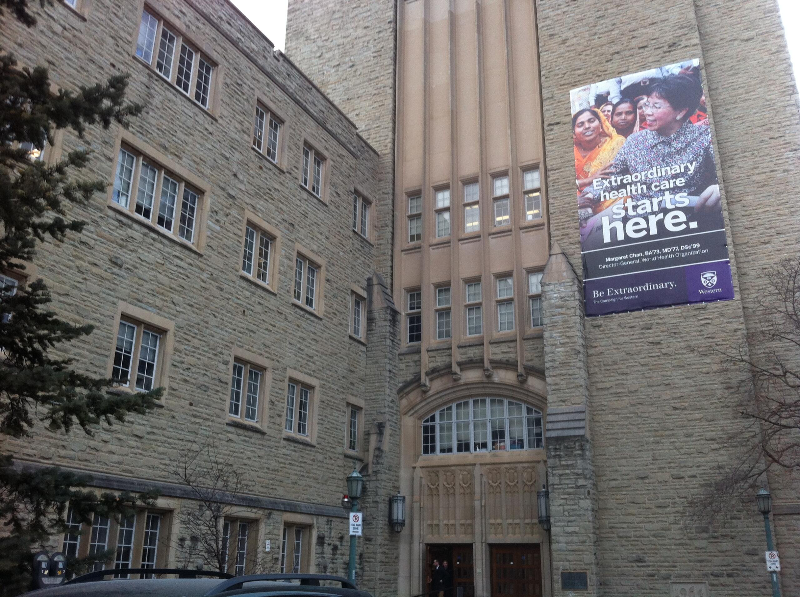 A stone building featuring large windows, an arched entrance, and a prominent banner promoting health care initiatives.