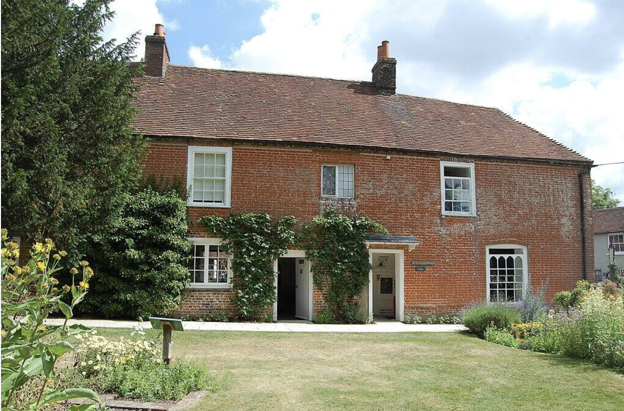 A charming red-brick house surrounded by greenery and flowers.