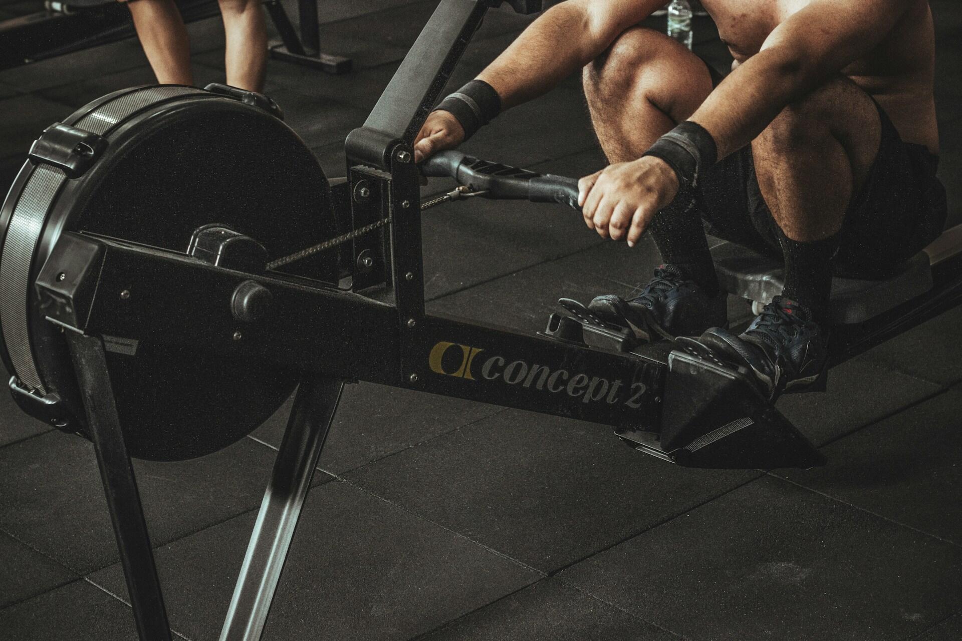 A close-up of a muscular person rowing on a Concept2 rowing machine in a gym, emphasizing the focus on fitness and strength training.