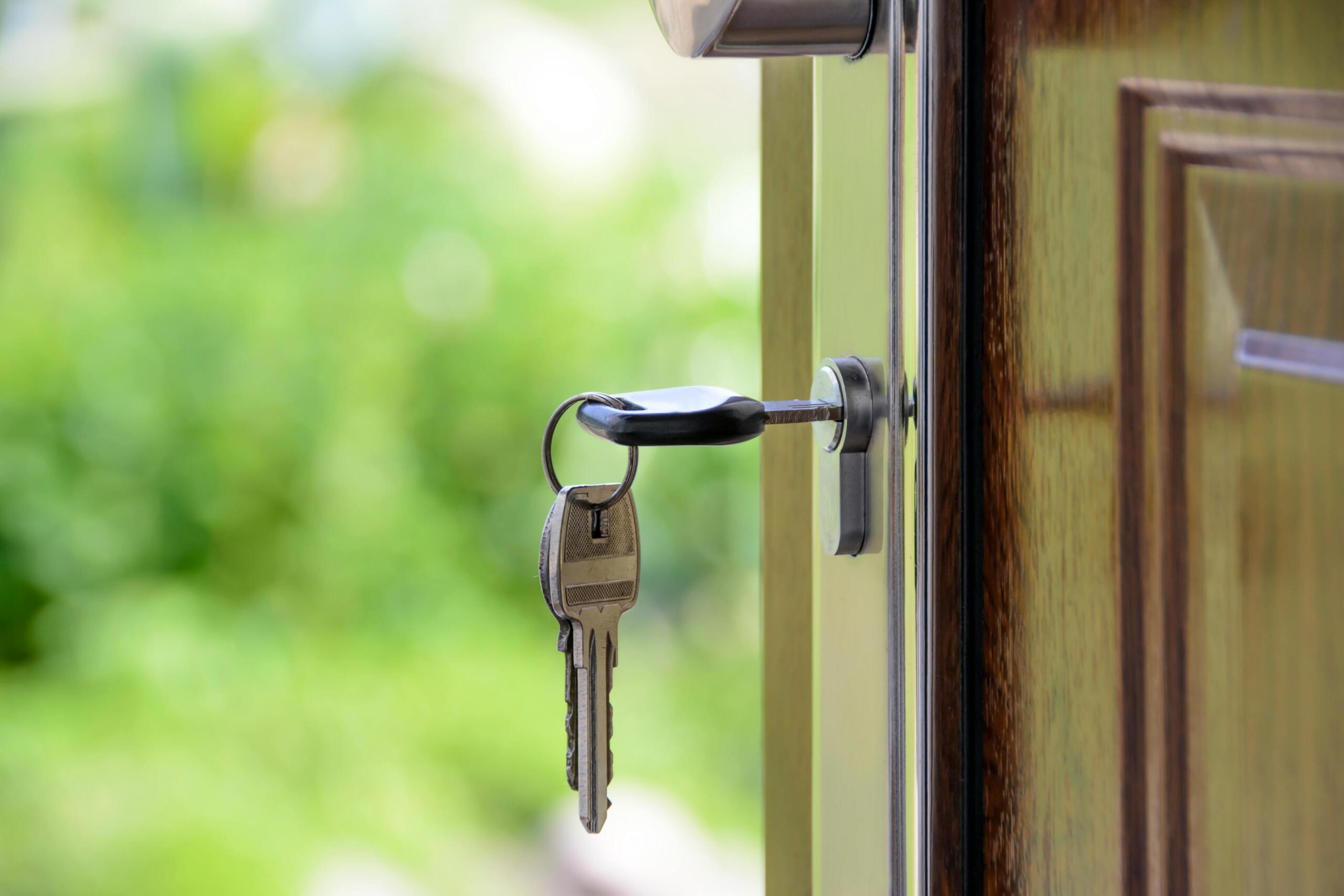 A close-up of a key inserted in a door lock, with a blurred green background suggesting an outdoor setting.