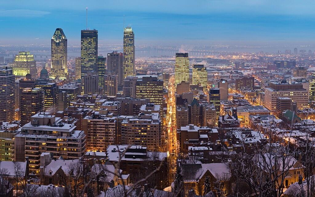 A panoramic view of a snowy Montreal skyline at dusk, showcasing illuminated skyscrapers and city streets.
