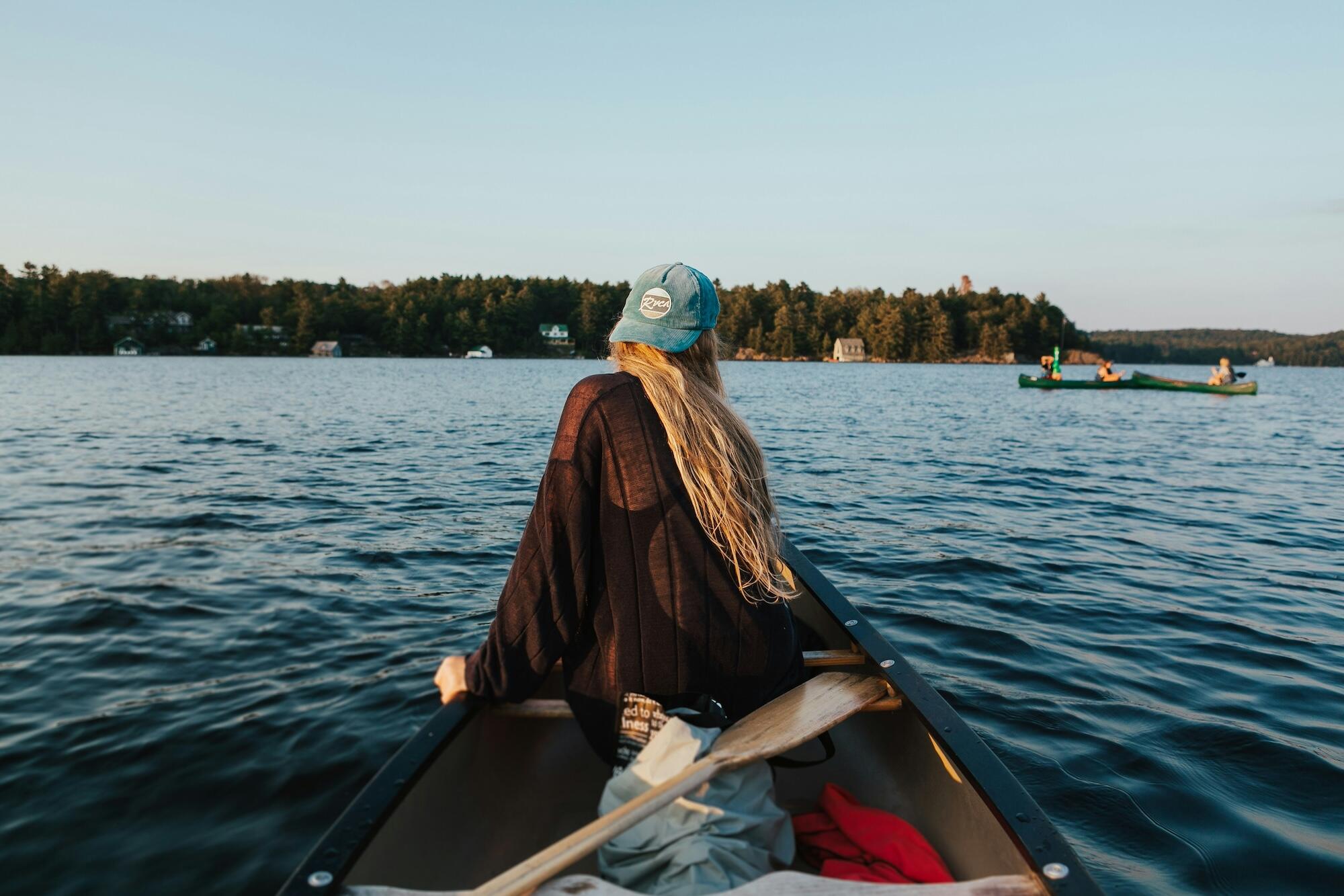 A woman in a canoe glides over a tranquil lake, enjoying the peaceful scenery around her.
