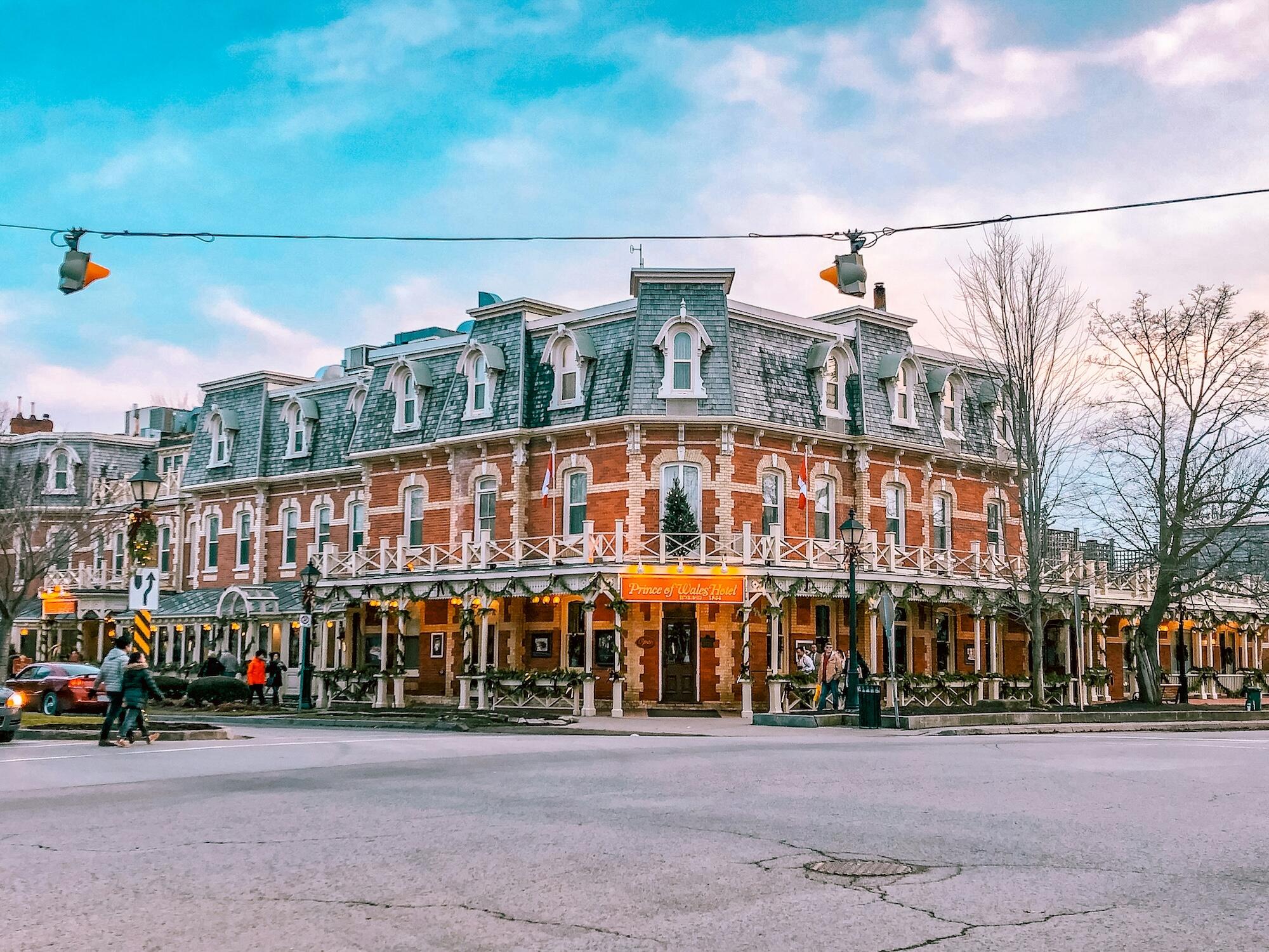 Historic brick hotel with Victorian architecture, warm lights, and surrounding trees, set against a pastel sky at dusk.