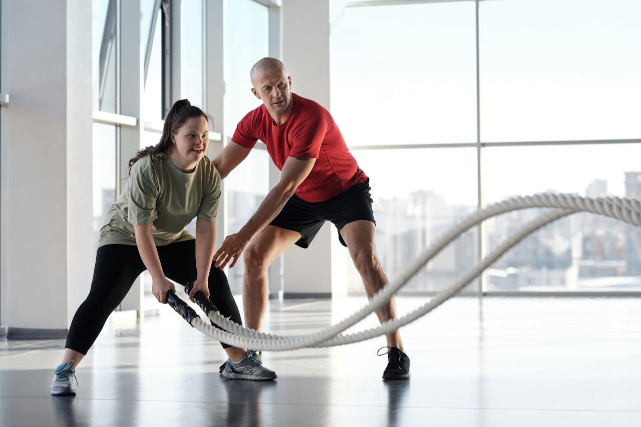 A trainer assists a woman using battle ropes in a bright, modern gym, focusing on fitness and technique.