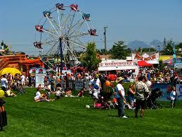 A lively fair scene with a Ferris wheel, food stands, and crowds of people enjoying games and activities on a sunny day.