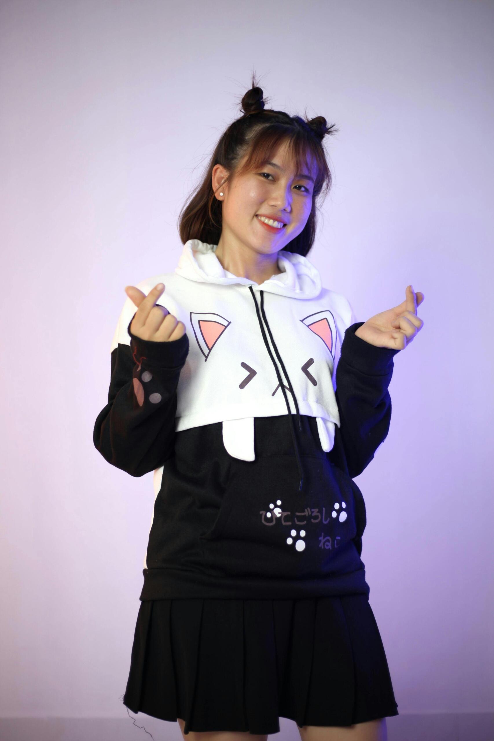 K-pop fan wearing a kitten outfit, smiling and making heart shapes with her hands at a music event. Source: TH Team.