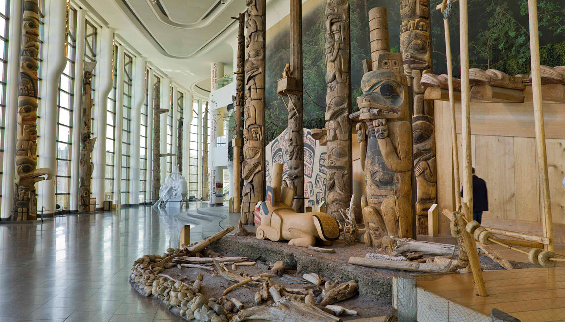 Photograph showing an exhibition hall displaying various wooden totem poles from ancient Canadian civilizations at the Canadian Museum of History.