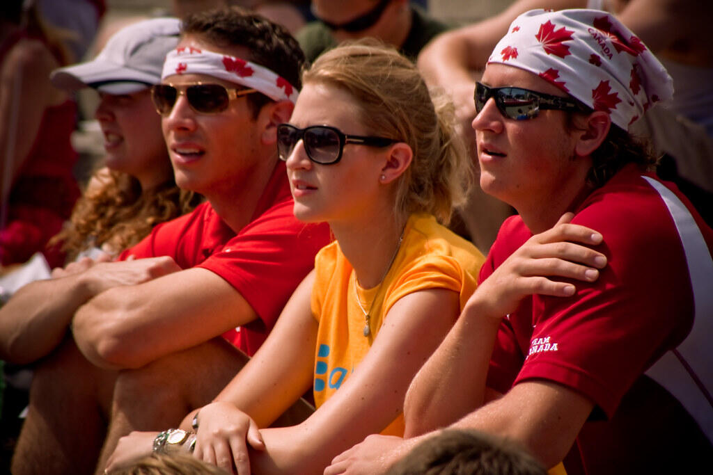 Group of people sitting closely together, wearing casual attire in bright colors, enjoying an outdoor event.