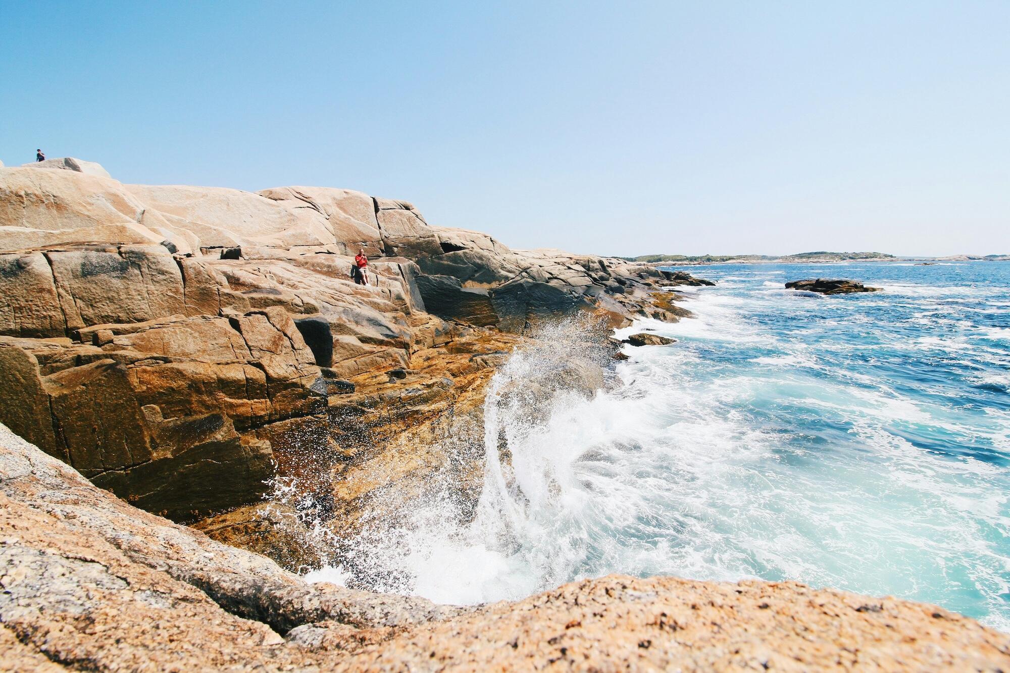 People stand on rocky outcrops by the ocean, gazing at the waves and enjoying the coastal scenery.