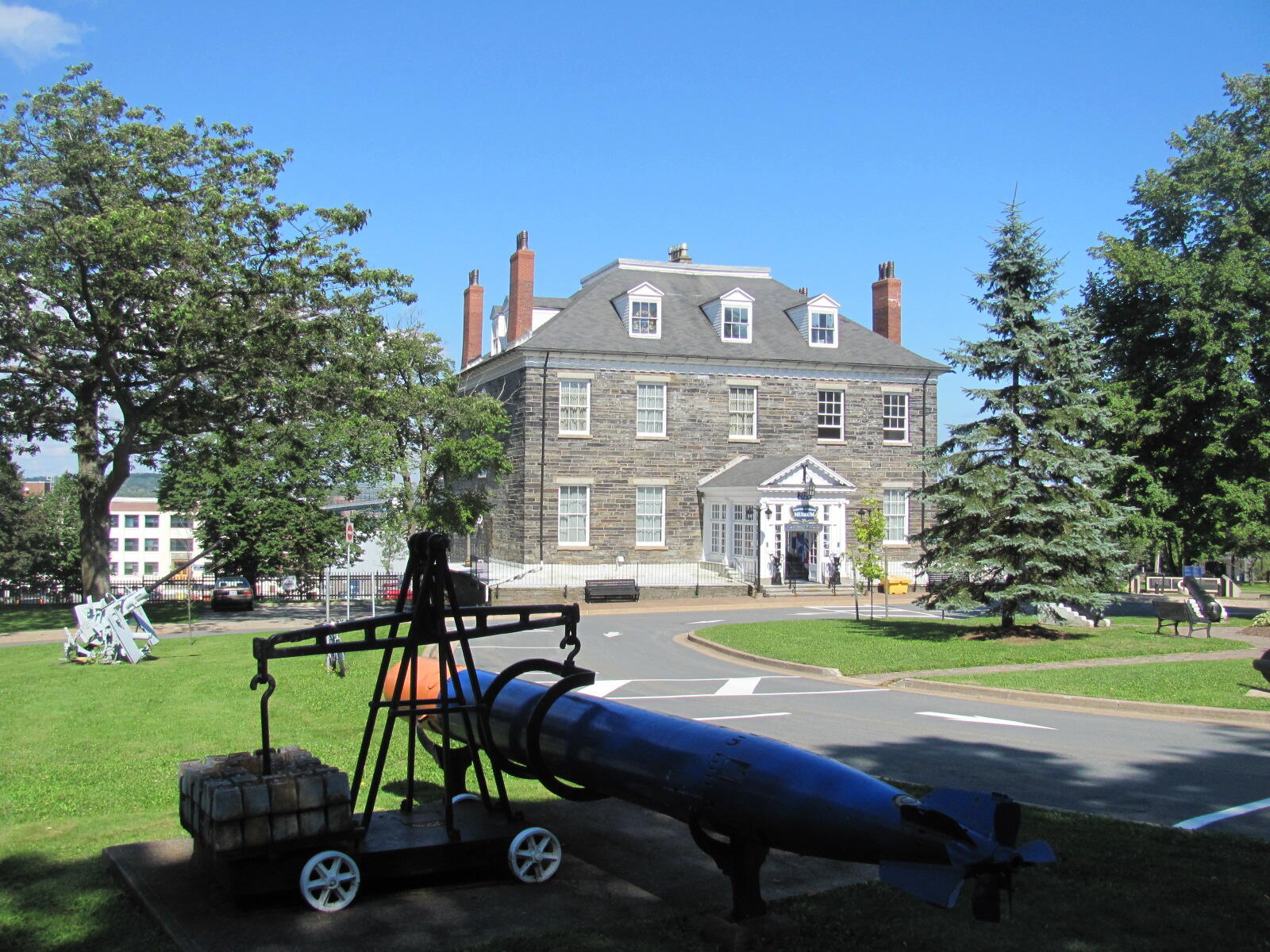 Historic stone building with a blue torpedo on display in the foreground, surrounded by trees and a clear blue sky.