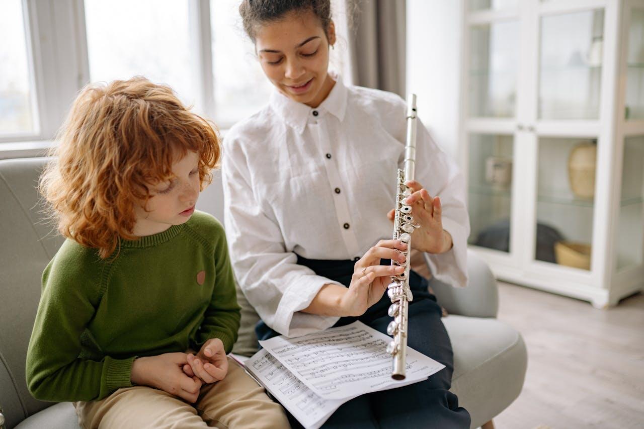 A woman teaches a child to play the flute, surrounded by sheet music in a bright, cozy indoor setting.