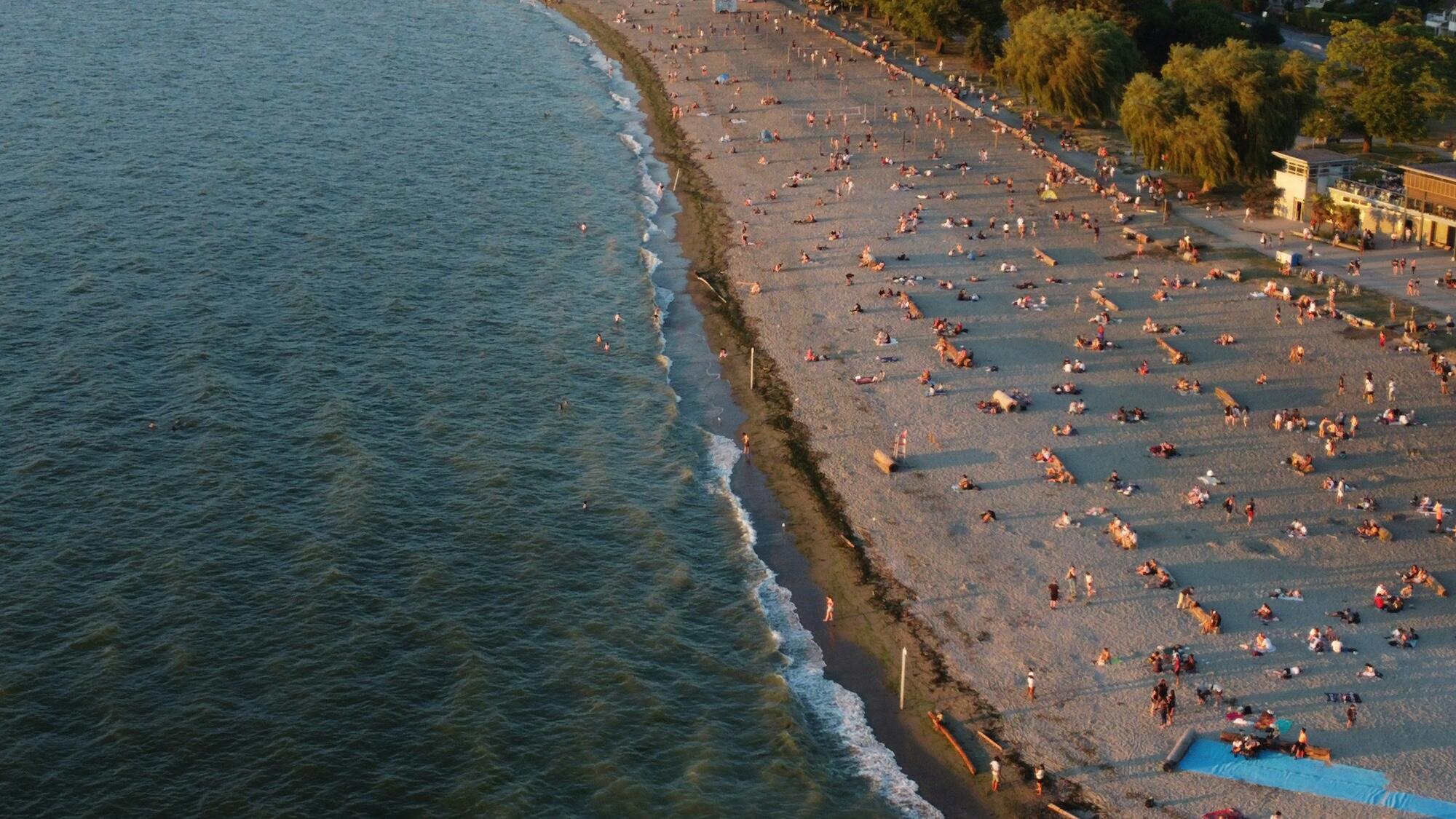 Aerial perspective of a vibrant summer beach scene, featuring numerous people enjoying the sun and surf.