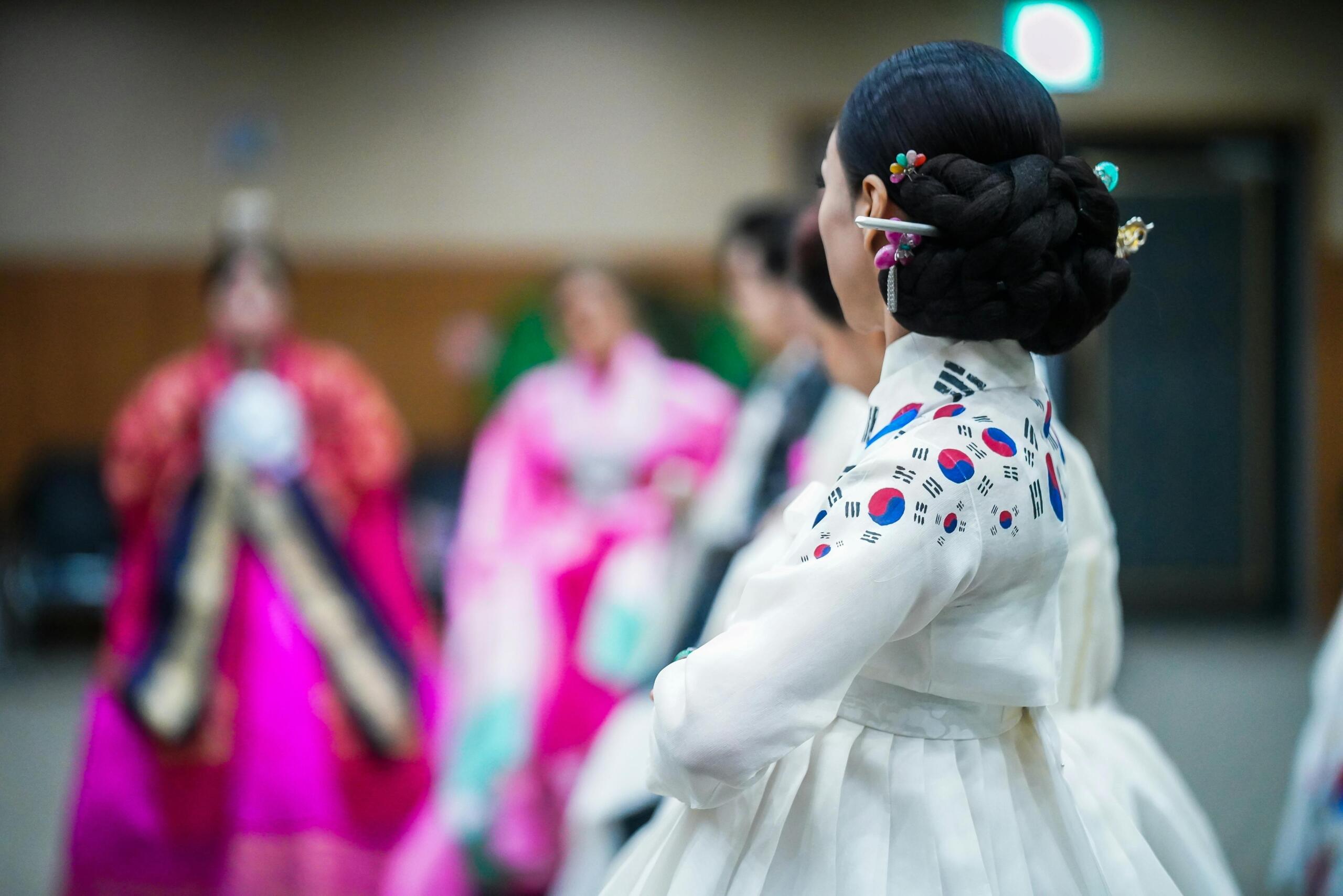 Korean women wearing colourful hanbok, with one adorned with South Korean flags during a cultural celebration.