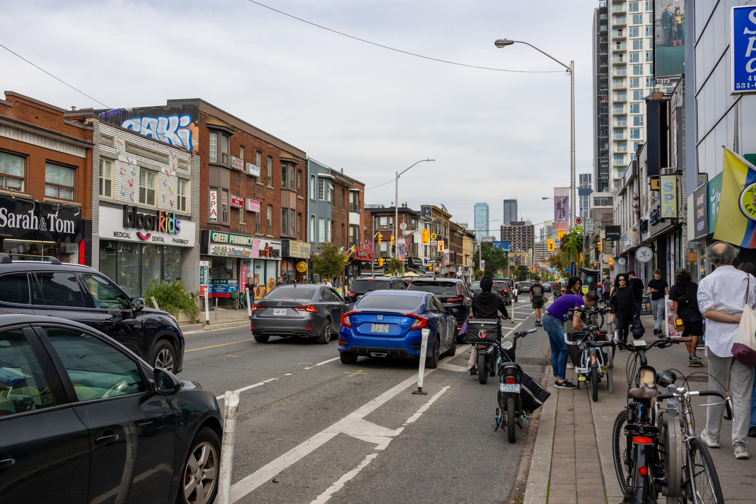 Summer streetscape of Toronto Koreatown with busy sidewalks, Korean storefronts, festival banners, and pedestrians enjoying the warm weather.