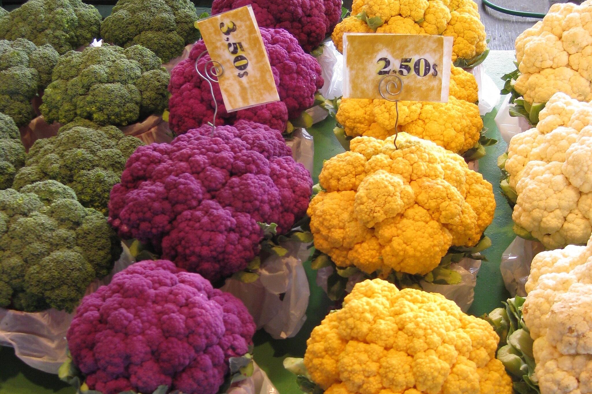 A cluster of fresh cauliflower heads with green leaves, arranged together on a white background.