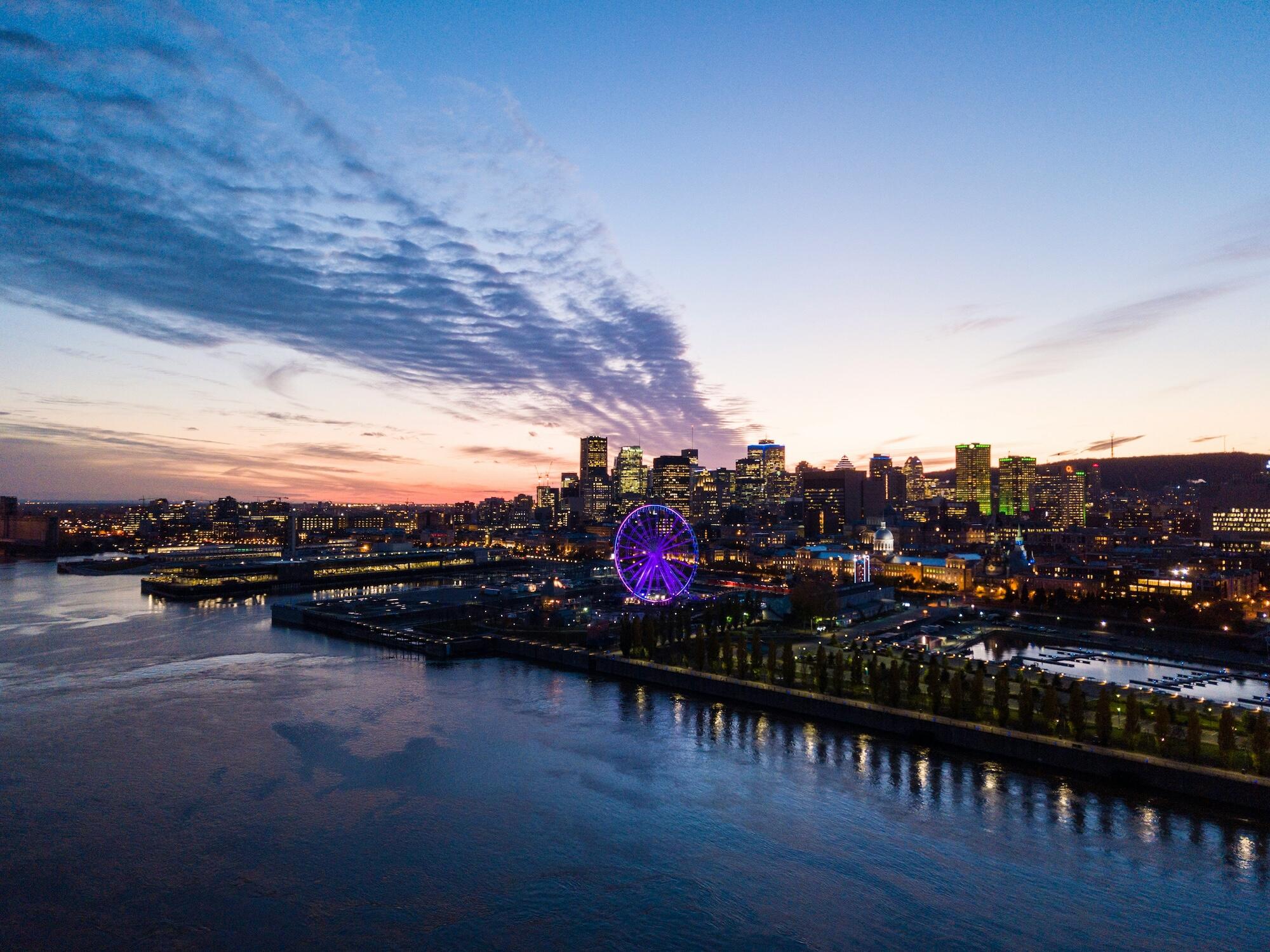 Sunset casts a warm glow over a city skyline, with a ferris wheel prominently displayed in the foreground.