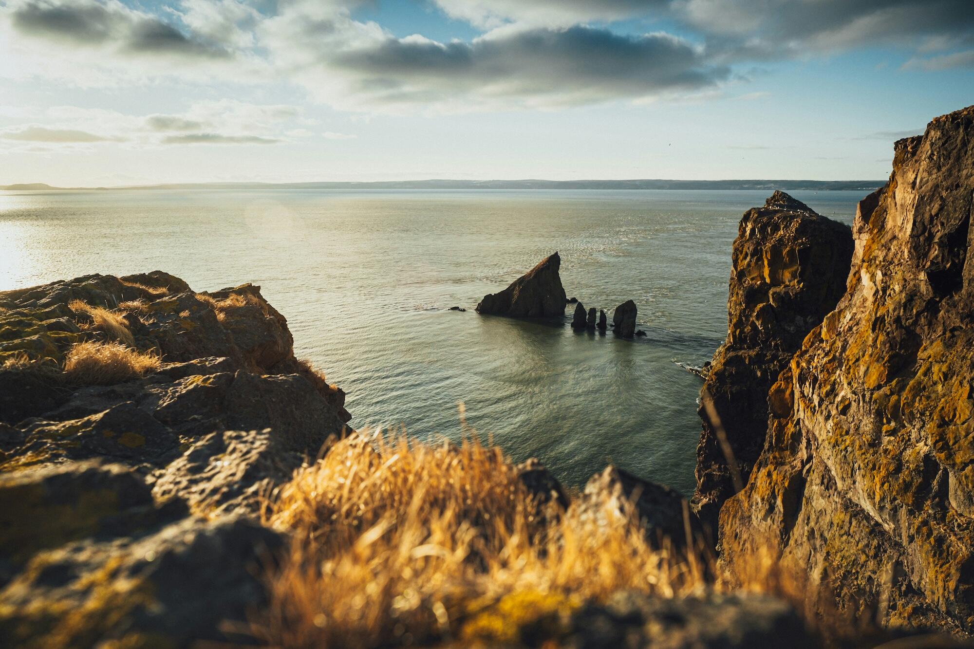 A panoramic view of the ocean from a high cliff, showcasing waves crashing against the rocky shore below.