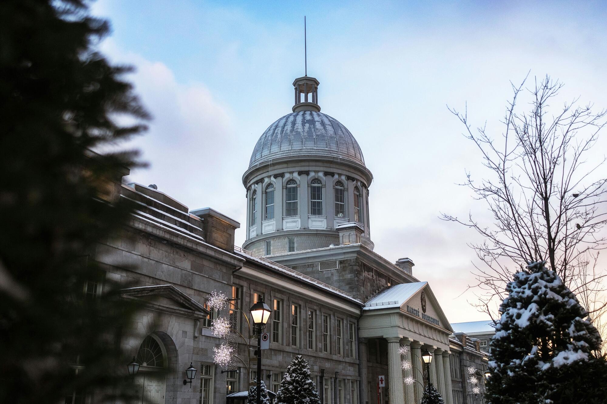 Historic building with a domed roof, surrounded by snow, decorated with lights, under a partially cloudy sky at dusk.
