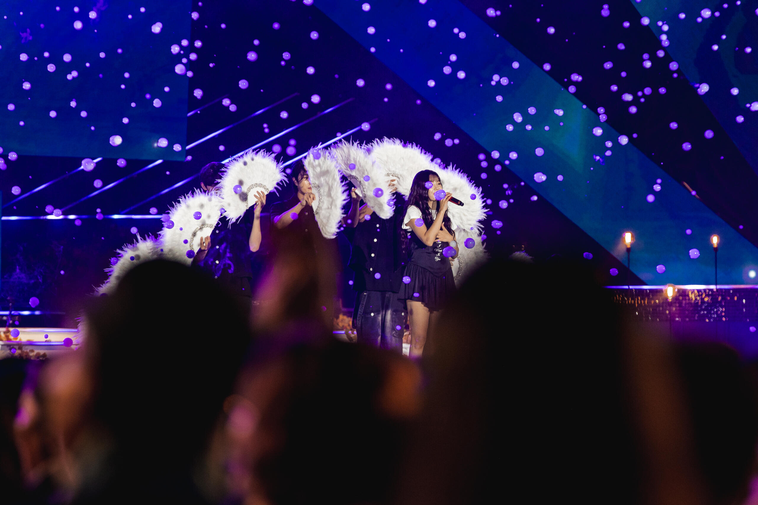 K-pop performers on stage under purple light effects, delivering a high-energy live dance performance at a cultural event.